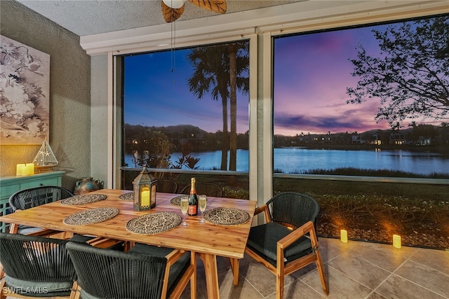 tiled dining space featuring a textured ceiling, a water view, and ceiling fan