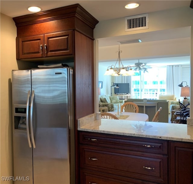 kitchen with light stone counters, stainless steel fridge, decorative light fixtures, and ceiling fan with notable chandelier