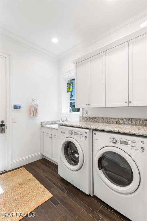 clothes washing area featuring cabinets, ornamental molding, washer and clothes dryer, dark wood-type flooring, and sink