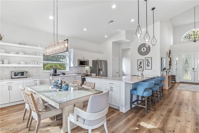 kitchen with a center island with sink, white cabinets, light hardwood / wood-style flooring, decorative light fixtures, and stainless steel appliances