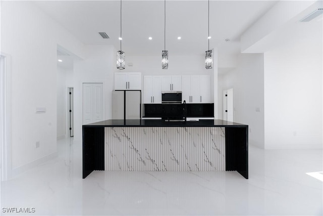 kitchen with a kitchen island with sink, sink, hanging light fixtures, white fridge, and white cabinetry