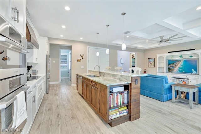 kitchen featuring coffered ceiling, white cabinetry, hanging light fixtures, an island with sink, and beamed ceiling