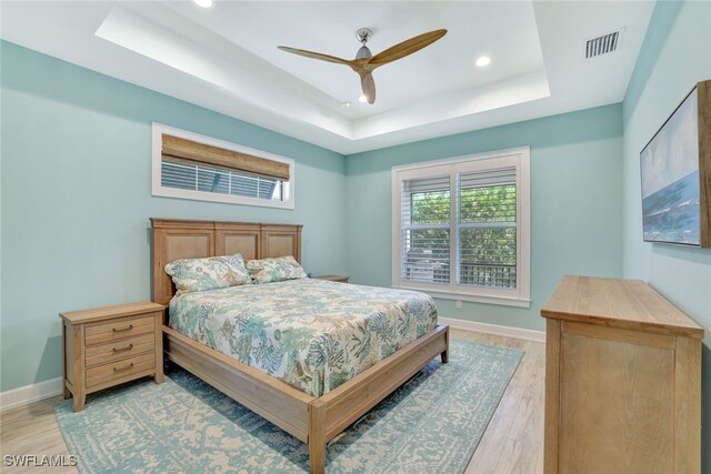 bedroom with ceiling fan, a raised ceiling, and light hardwood / wood-style flooring