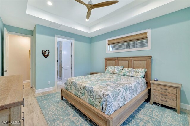 bedroom featuring a tray ceiling, light hardwood / wood-style floors, ceiling fan, and ensuite bathroom