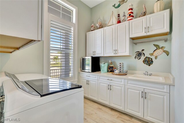 kitchen featuring washing machine and dryer, sink, white cabinets, and light hardwood / wood-style flooring