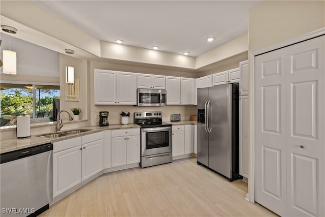 kitchen with white cabinets, hanging light fixtures, sink, light hardwood / wood-style flooring, and appliances with stainless steel finishes