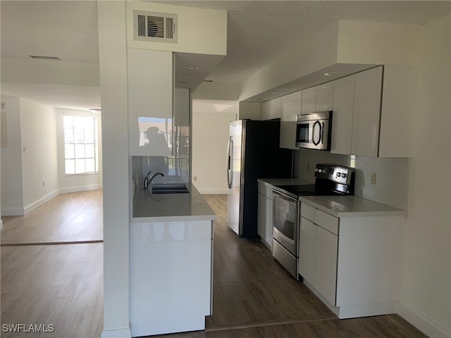 kitchen featuring appliances with stainless steel finishes, a textured ceiling, dark wood-type flooring, sink, and white cabinets