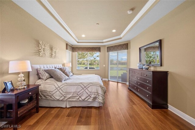 bedroom with hardwood / wood-style flooring, a raised ceiling, and crown molding