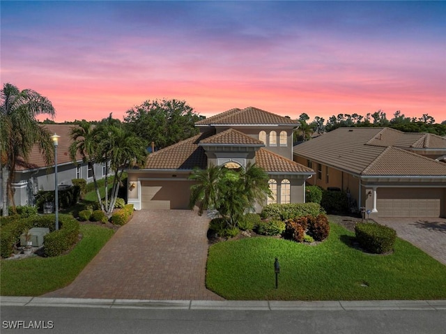 mediterranean / spanish-style home with decorative driveway, stucco siding, an attached garage, a front yard, and a tiled roof