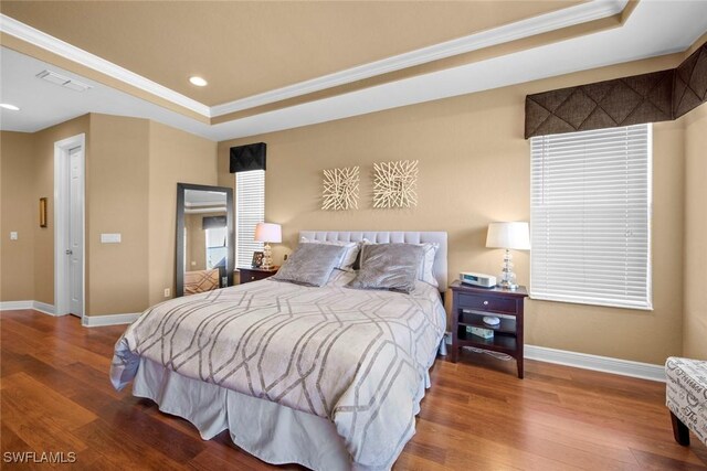 bedroom with a raised ceiling, crown molding, and hardwood / wood-style flooring