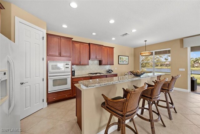 kitchen with a kitchen bar, a kitchen island, hanging light fixtures, and white appliances