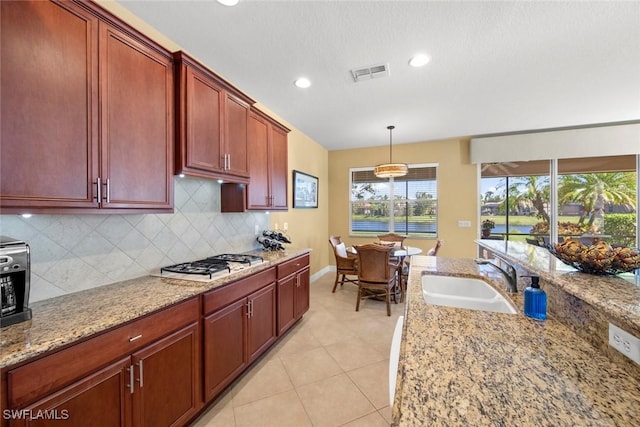 kitchen with light stone countertops, sink, pendant lighting, and stainless steel gas stovetop