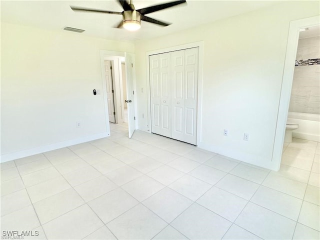 unfurnished bedroom featuring ceiling fan, ensuite bath, light tile patterned floors, and a closet