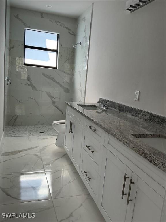 bathroom featuring a tile shower, vanity, and toilet