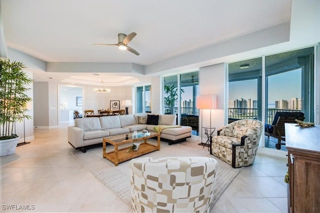 living room with ceiling fan with notable chandelier and a raised ceiling