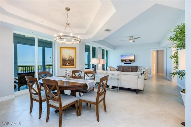 dining room with ceiling fan with notable chandelier and a raised ceiling