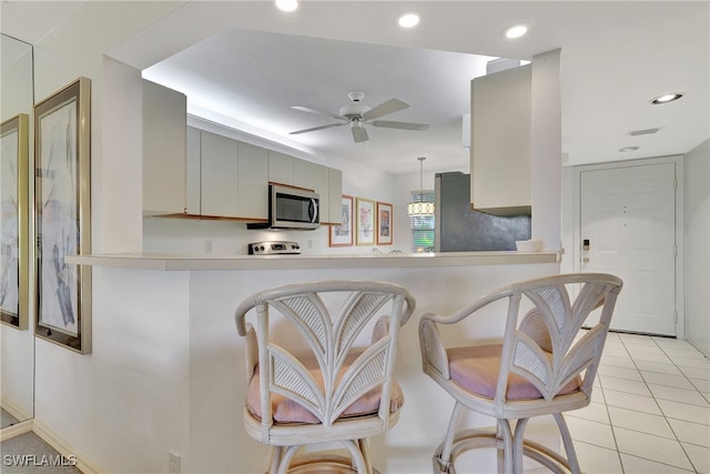 kitchen featuring ceiling fan, stainless steel appliances, kitchen peninsula, a breakfast bar area, and light tile patterned floors