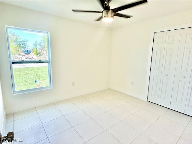 unfurnished bedroom with ceiling fan, a closet, light tile patterned floors, and multiple windows