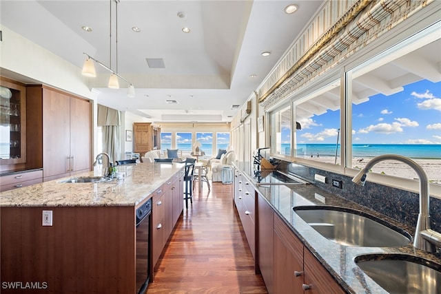 kitchen featuring dark hardwood / wood-style flooring, stone counters, a center island with sink, and a water view