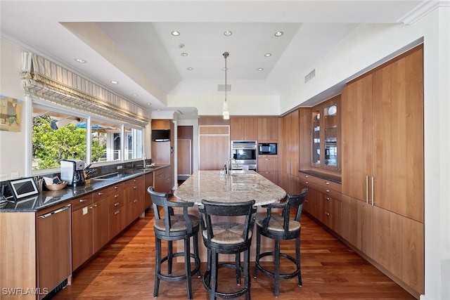 kitchen with black microwave, sink, dark hardwood / wood-style floors, dark stone countertops, and a spacious island