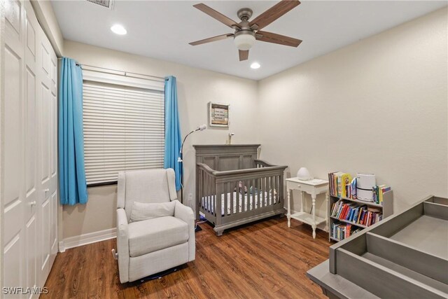 bedroom with a nursery area, a closet, ceiling fan, and dark wood-type flooring