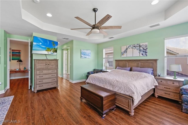 bedroom with dark hardwood / wood-style floors, ceiling fan, and a tray ceiling