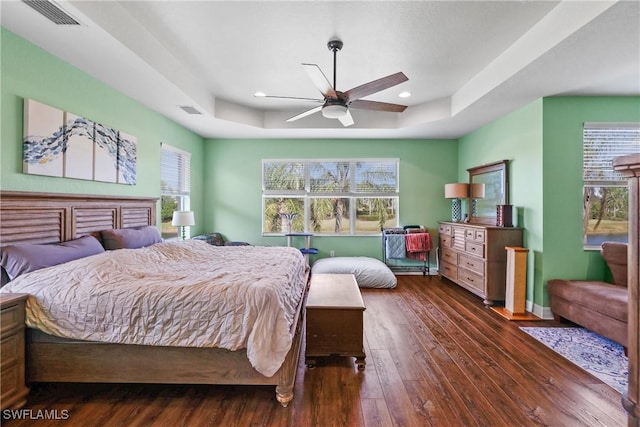 bedroom featuring a raised ceiling, ceiling fan, dark hardwood / wood-style flooring, and multiple windows