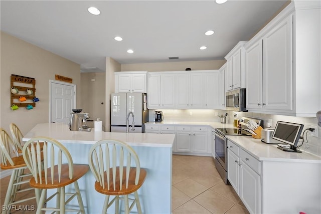 kitchen with appliances with stainless steel finishes, a kitchen breakfast bar, a center island with sink, white cabinetry, and light tile patterned flooring