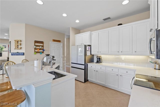 kitchen featuring white cabinetry, sink, stainless steel appliances, a kitchen bar, and light tile patterned flooring