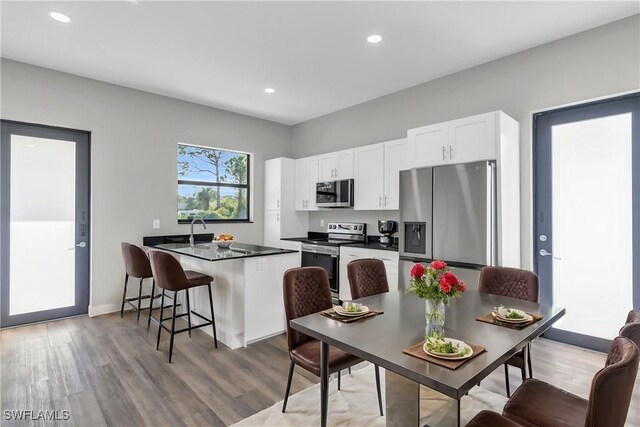 kitchen with kitchen peninsula, appliances with stainless steel finishes, a breakfast bar area, white cabinets, and hardwood / wood-style flooring