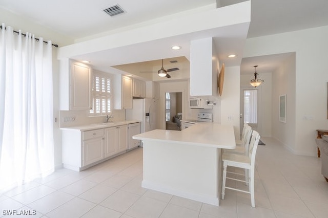 kitchen with white appliances, ceiling fan with notable chandelier, sink, light tile patterned floors, and white cabinets