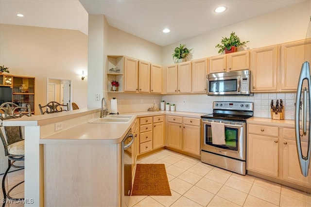 kitchen featuring sink, light brown cabinetry, appliances with stainless steel finishes, a kitchen bar, and kitchen peninsula