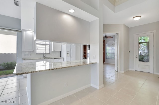kitchen featuring light stone counters, sink, white refrigerator with ice dispenser, white cabinets, and plenty of natural light