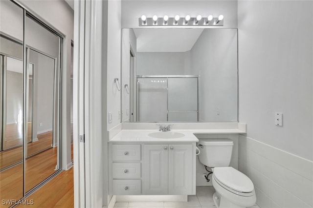bathroom with vanity, hardwood / wood-style flooring, toilet, tile walls, and a shower with shower door