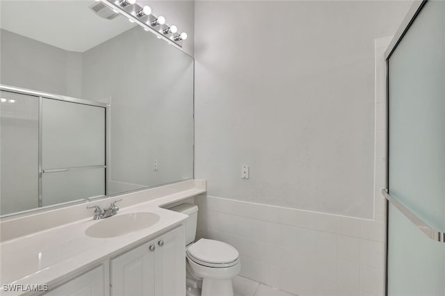 bathroom with vanity, toilet, tile walls, and a shower with shower door
