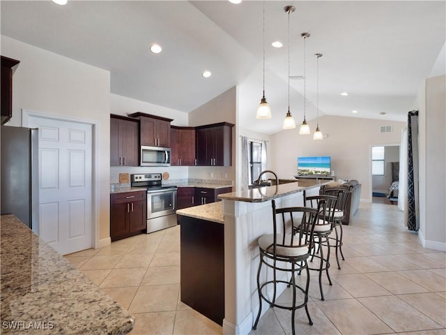 kitchen featuring appliances with stainless steel finishes, light stone counters, hanging light fixtures, lofted ceiling, and an island with sink