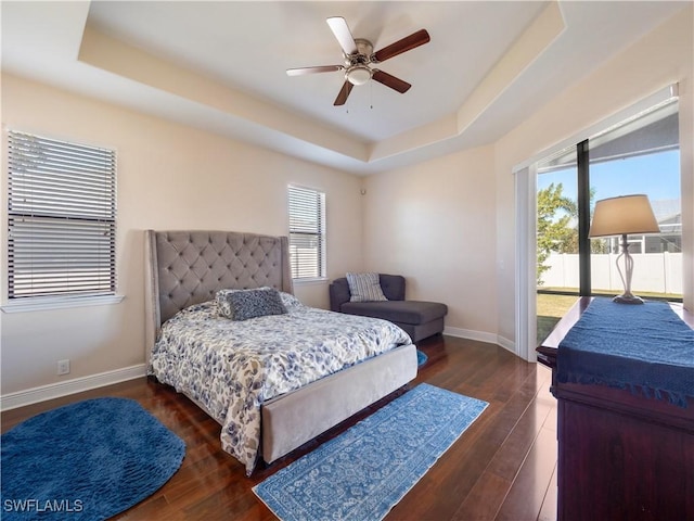 bedroom with dark hardwood / wood-style floors, ceiling fan, multiple windows, and a tray ceiling