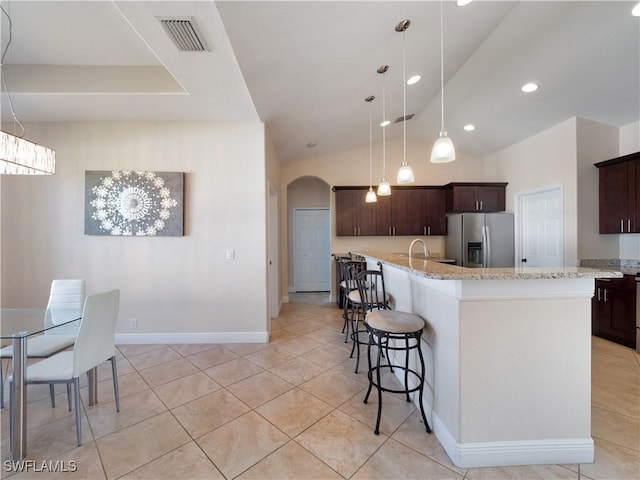 kitchen with stainless steel refrigerator with ice dispenser, dark brown cabinets, vaulted ceiling, a kitchen island with sink, and pendant lighting