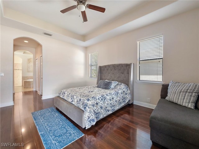 bedroom with dark hardwood / wood-style floors, ensuite bath, a raised ceiling, and ceiling fan