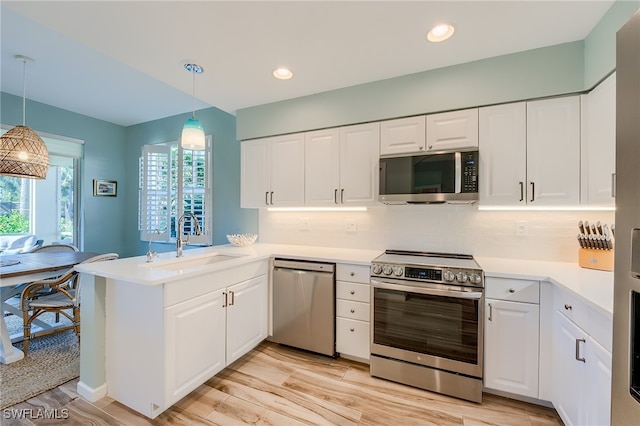 kitchen featuring white cabinetry, sink, stainless steel appliances, kitchen peninsula, and decorative light fixtures