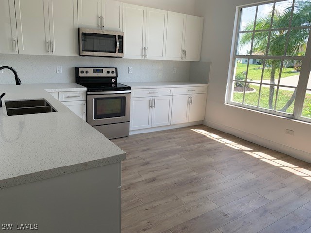 kitchen with sink, light hardwood / wood-style flooring, light stone countertops, appliances with stainless steel finishes, and white cabinetry