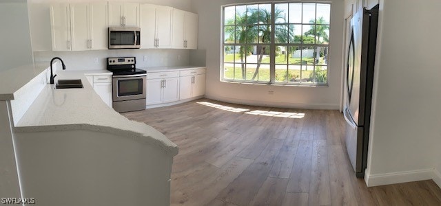 kitchen featuring sink, light hardwood / wood-style flooring, light stone countertops, appliances with stainless steel finishes, and white cabinetry