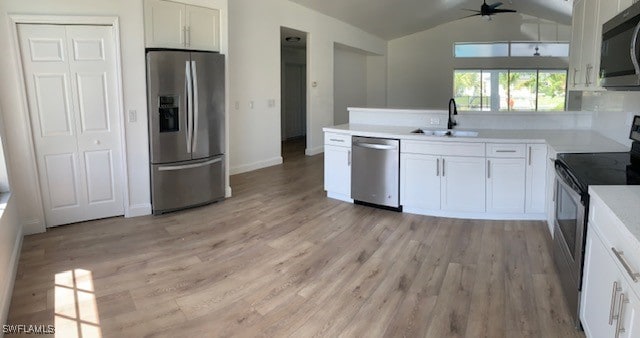 kitchen featuring white cabinets, sink, vaulted ceiling, light wood-type flooring, and stainless steel appliances