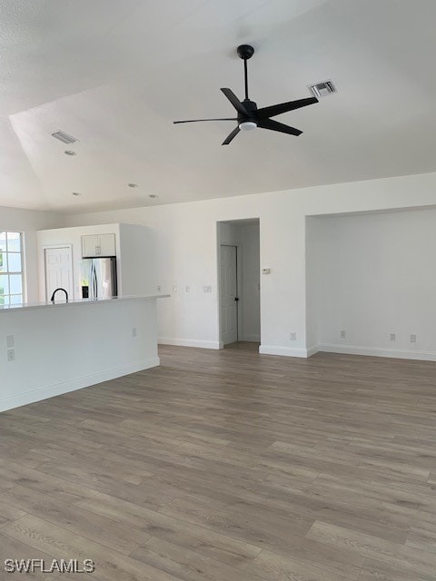 unfurnished living room with ceiling fan, light wood-type flooring, and vaulted ceiling