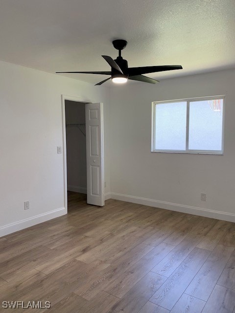 unfurnished bedroom with ceiling fan, a spacious closet, light wood-type flooring, a textured ceiling, and a closet