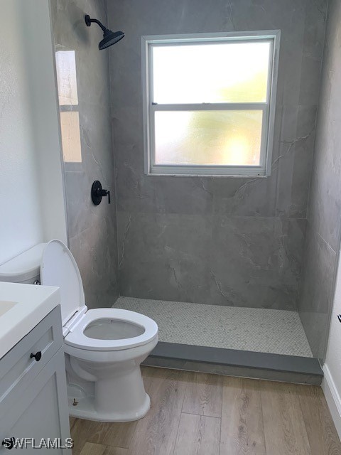 bathroom with tiled shower, wood-type flooring, vanity, and toilet