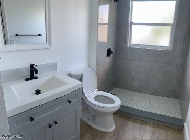 bathroom featuring toilet, wood-type flooring, vanity, and a tile shower