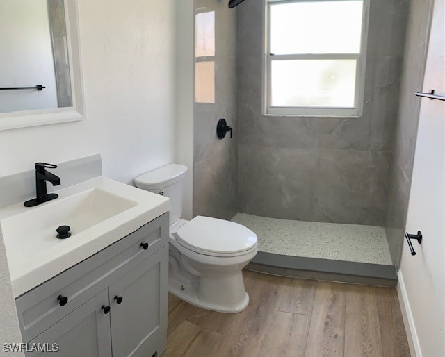 bathroom featuring a tile shower, toilet, vanity, and hardwood / wood-style flooring