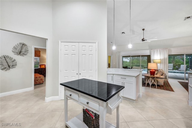 kitchen featuring a center island, a high ceiling, ceiling fan, light tile patterned flooring, and white cabinetry