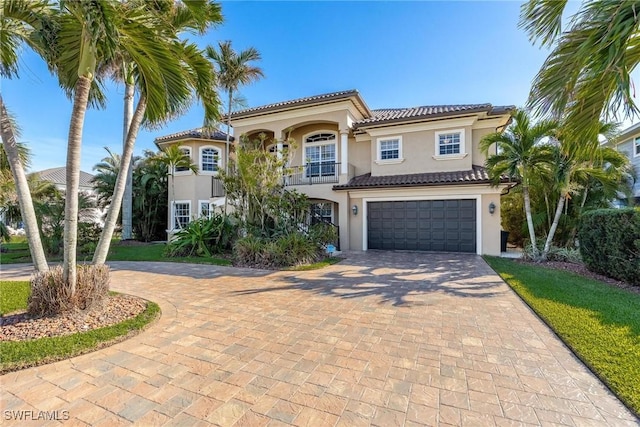 mediterranean / spanish home featuring decorative driveway, a tile roof, an attached garage, and stucco siding